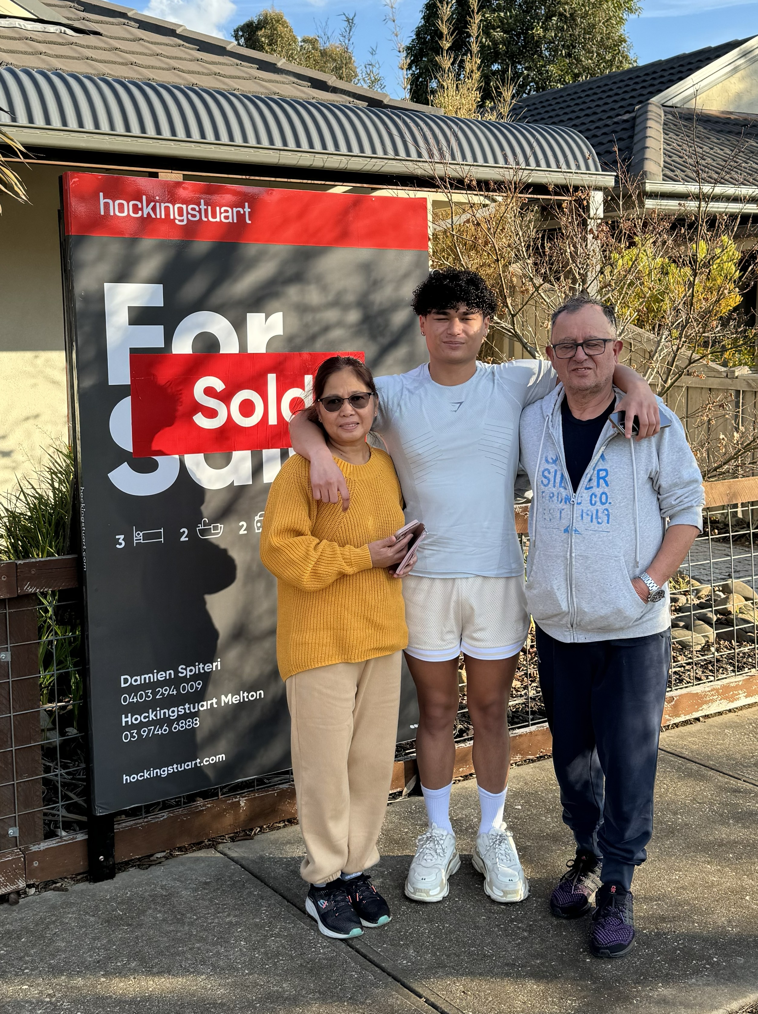 Jake with his parents in front of a sold Hockingstuart sign